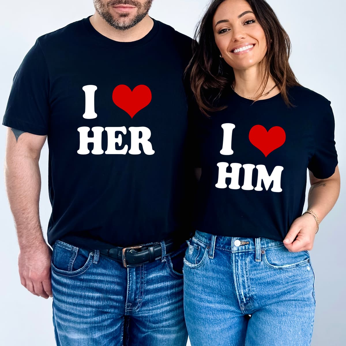 Cuplu purtând tricouri negre asortate cu mesajele „I love her” și „I love him”, ideale pentru seturi personalizate de cuplu