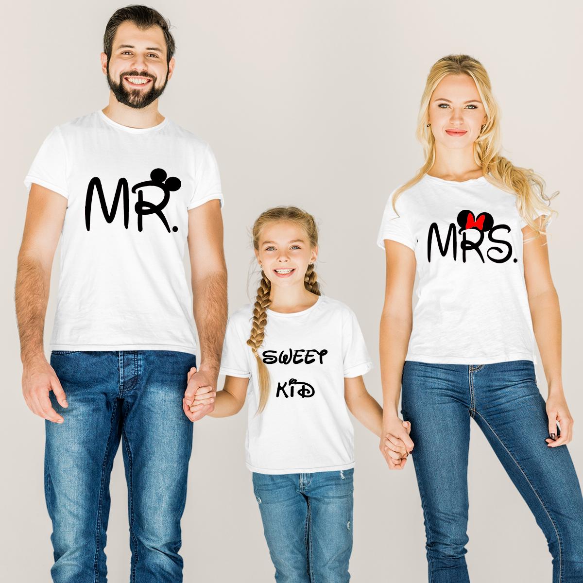 Set de trei tricouri albe pentru familie cu tematică inspirată de desene animate: tatăl poartă un tricou cu mesajul 'MR.' și urechi de mouse negre, mama poartă 'MRS.' cu urechi de mouse și fundă roșie, iar fetița poartă un tricou cu mesajul 'SWEET KID' în font stilizat.
