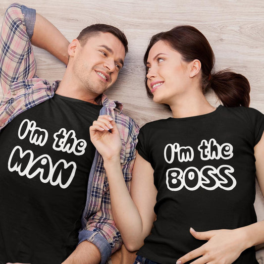 Cuplu tânăr stând întins pe podea, privindu-se cu dragoste, purtând un set de tricouri negre asortate; bărbatul poartă mesajul amuzant „I'm the MAN”, iar femeia poartă tricoul cu mesajul „I'm the BOSS”.