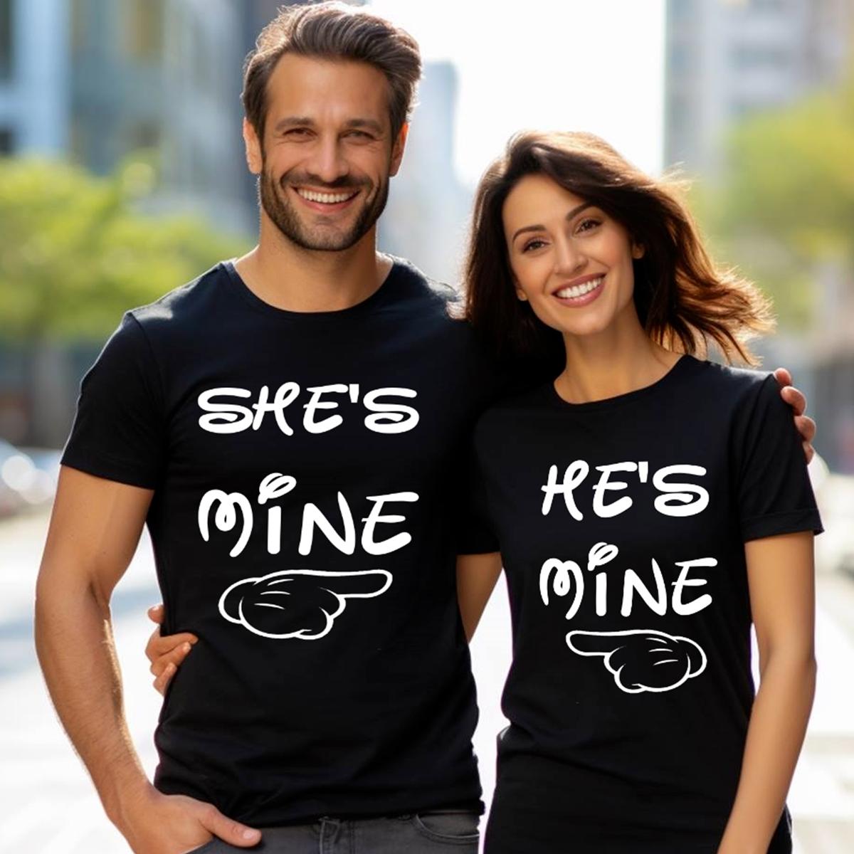 Set de două tricouri negre pentru cuplu cu mesajele albe She's Mine și He's Mine și grafică cu mână care indică partenerul, purtate de un cuplu zâmbitor.