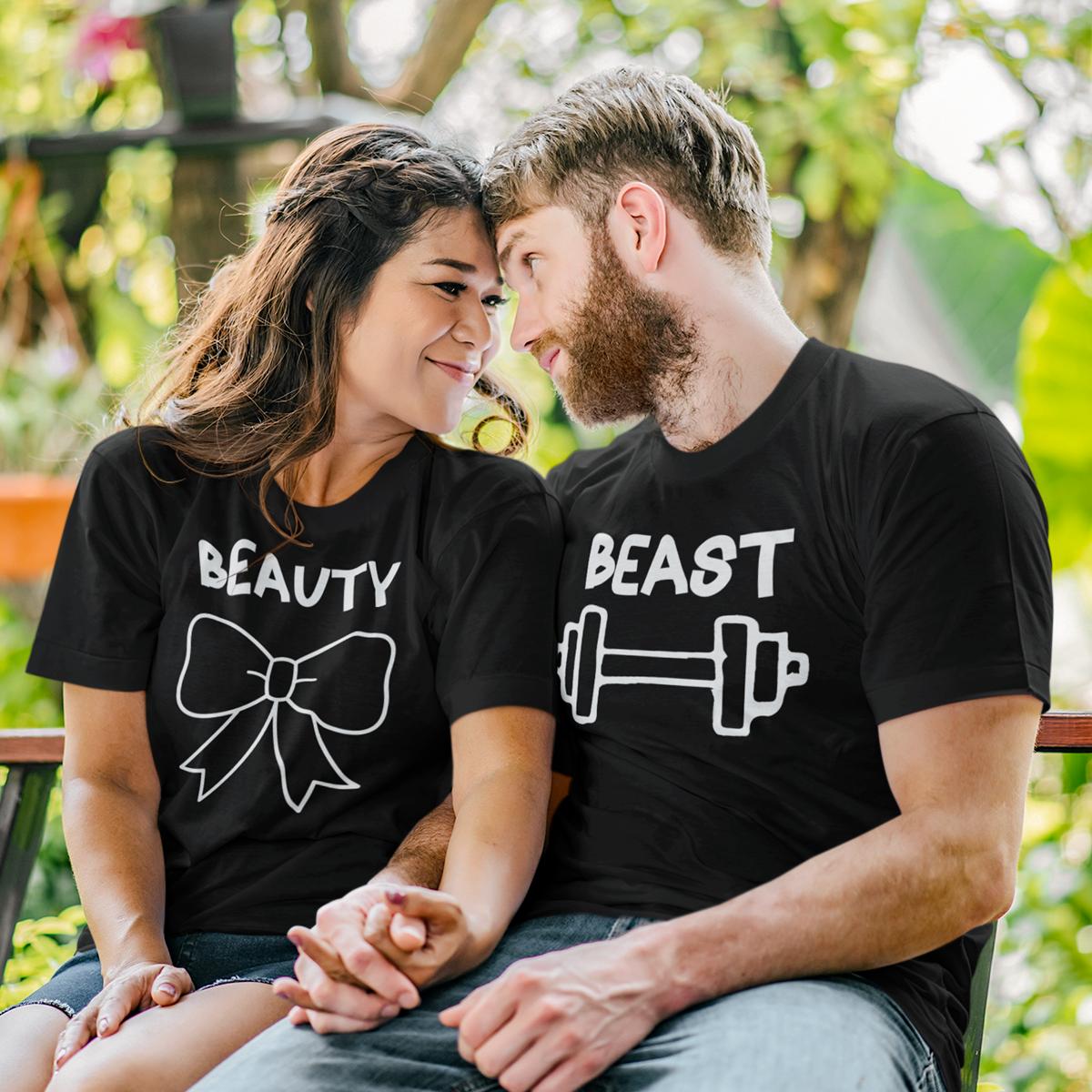 Set de două tricouri negre personalizate pentru cuplu, model 'Beauty and Beast' cu grafică fitness: tricou damă cu mesaj 'Beauty' și fundiță albă, tricou bărbat cu mesaj 'Beast' și simbol halteră, purtate de un cuplu într-un decor natural.